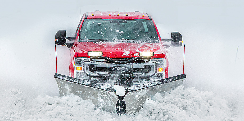 Ford Super Duty pickup stands read to clear snow with a red plow.
